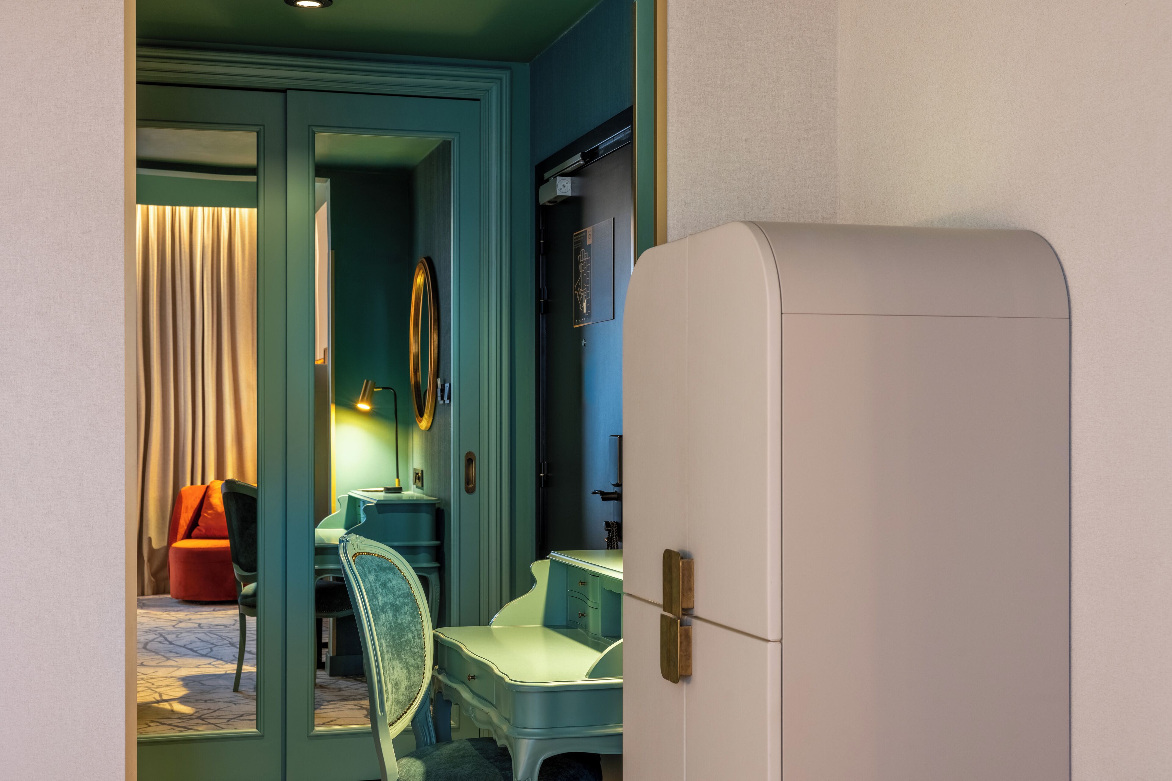 Una habitación con un escritorio de estilo vintage, una silla, una cama con cortina y un refrigerador blanco.