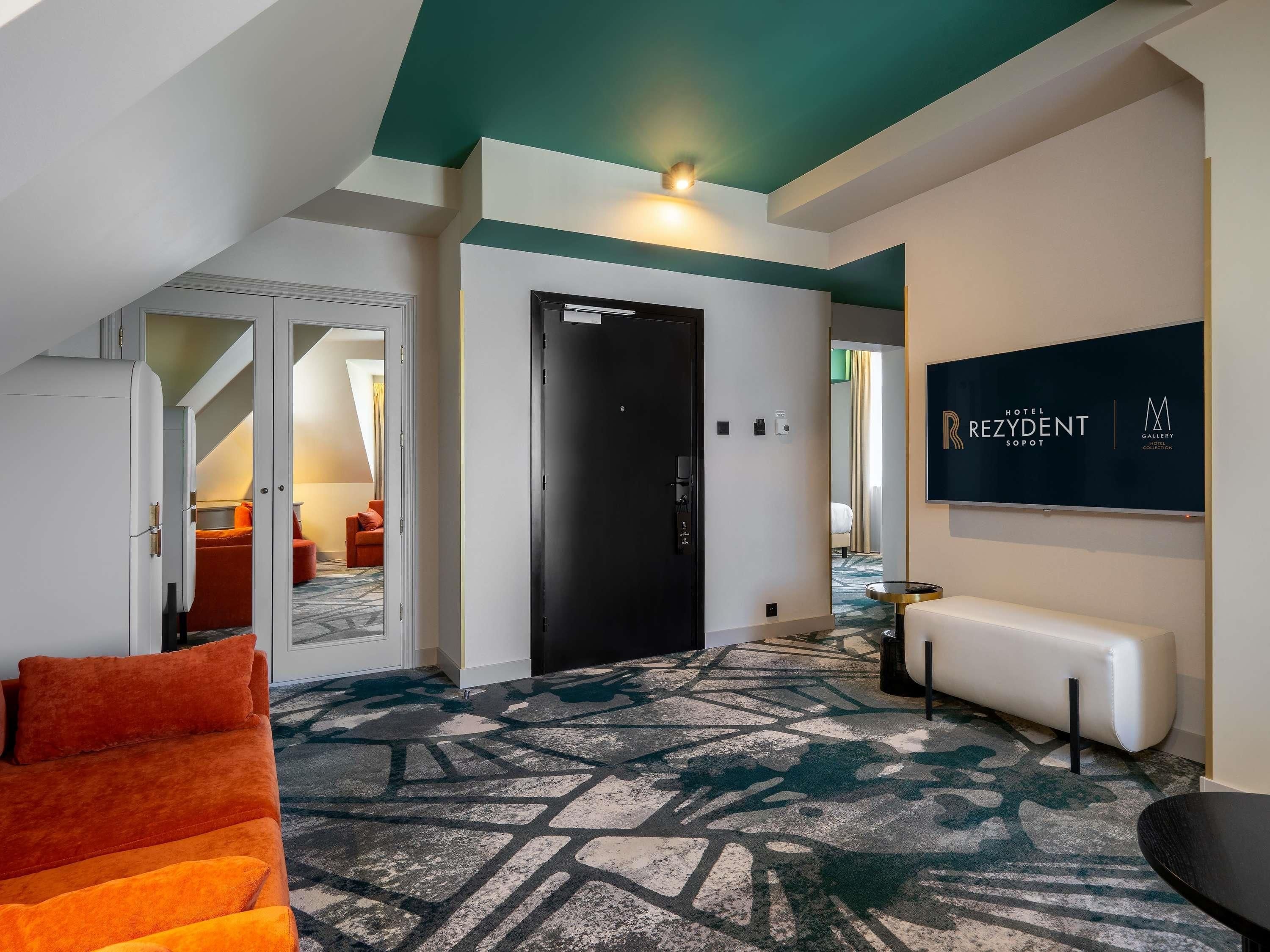 A hotel lobby with a modern design, including a patterned carpet, a bench, and a wall-mounted sign.