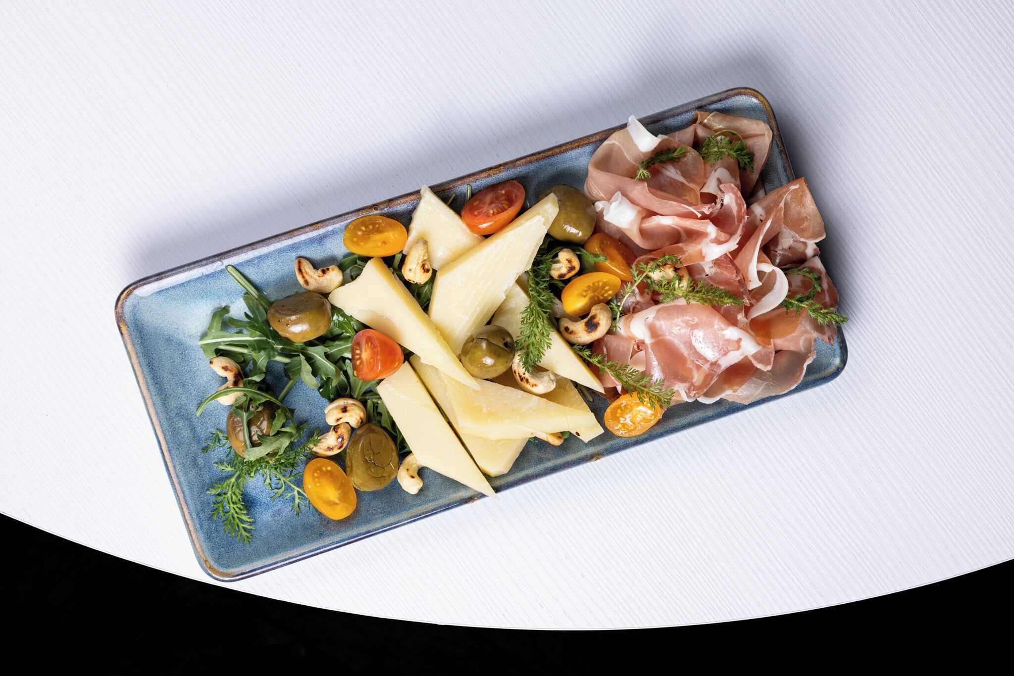 A rectangular glass dish with various food items including cheese, olives, tomatoes, and prosciutto.