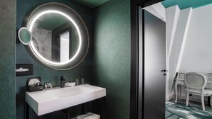 A modern bathroom with a white sink, a round mirror with a light, and a door leading to a bedroom. - Rezydent Hotel Sopot - MGallery Collection (Sopot)