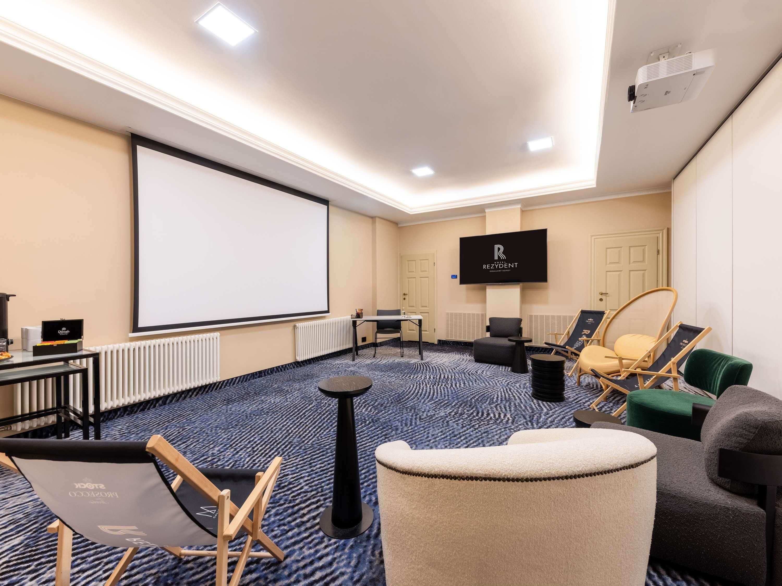 A conference room with a projector screen, a flat-screen TV, and a seating arrangement including chairs and a sofa.