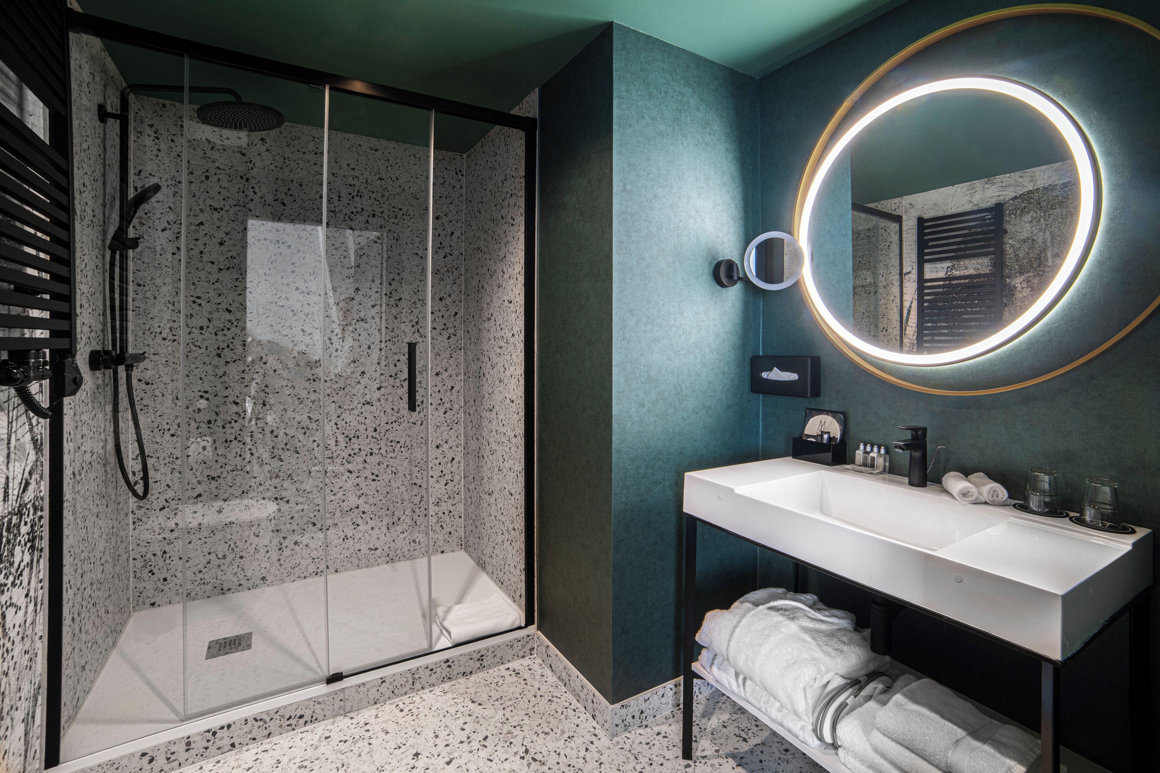 A modern bathroom with a glass-enclosed shower, a white sink with a mirror, and a towel rack.