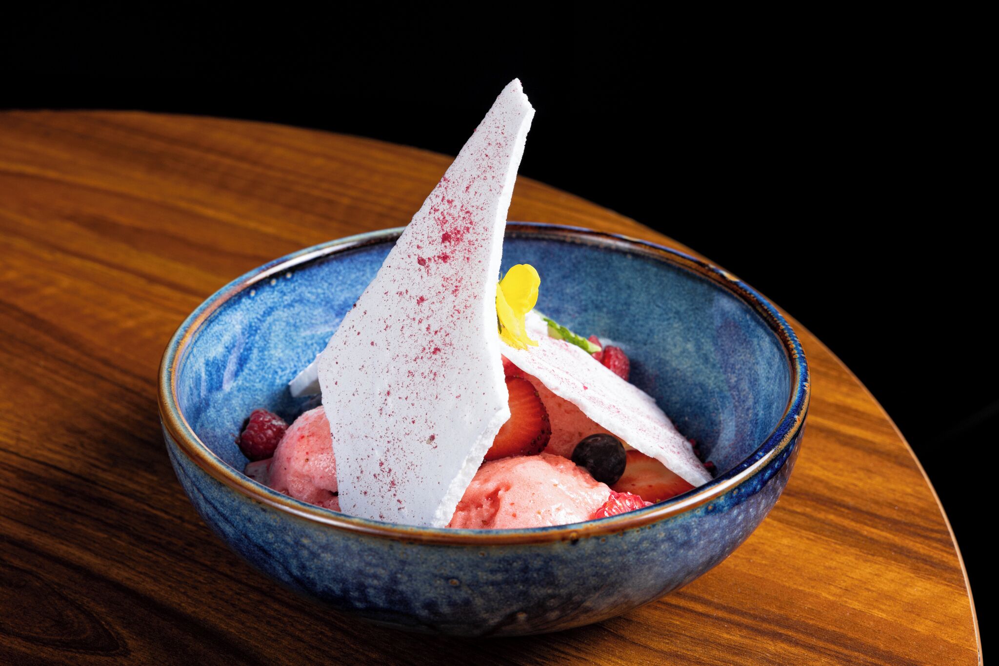 Een schaal dessert met ijs en bessen op een houten tafel.