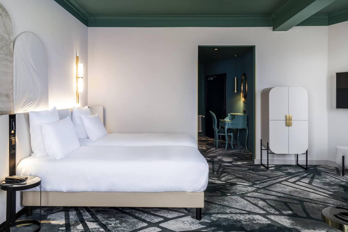 Ein Hotelzimmer mit Bett, Nachttisch, Lampe und einem gemusterten Teppich.