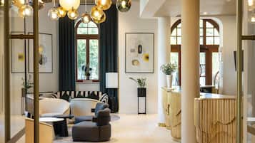Un interno moderno con una poltrona, poggiapiedi e un tavolo rotondo. Sono presenti lampade sferiche a sospensione e un colonnato in legno con listelli verticali.