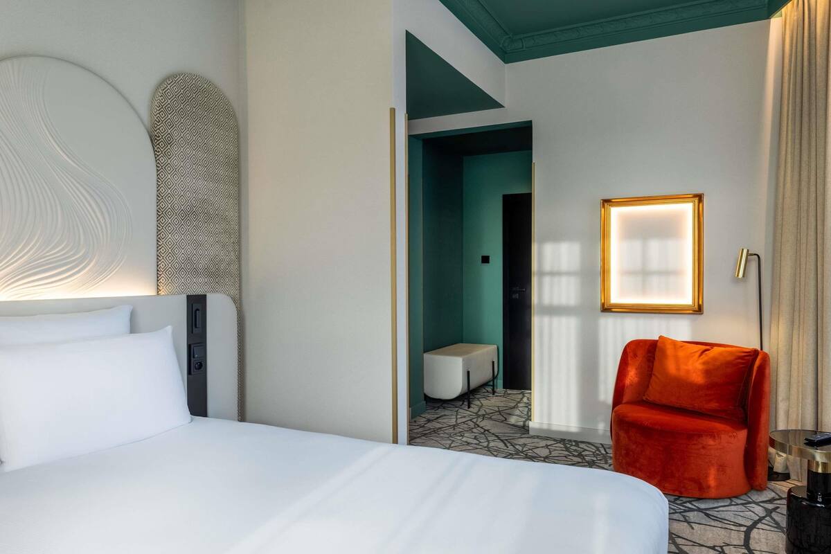 Ein Hotelzimmer mit einem großen Bett, einem roten Sessel, einem kleinen Tisch und einem gerahmten Bild an der Wand.