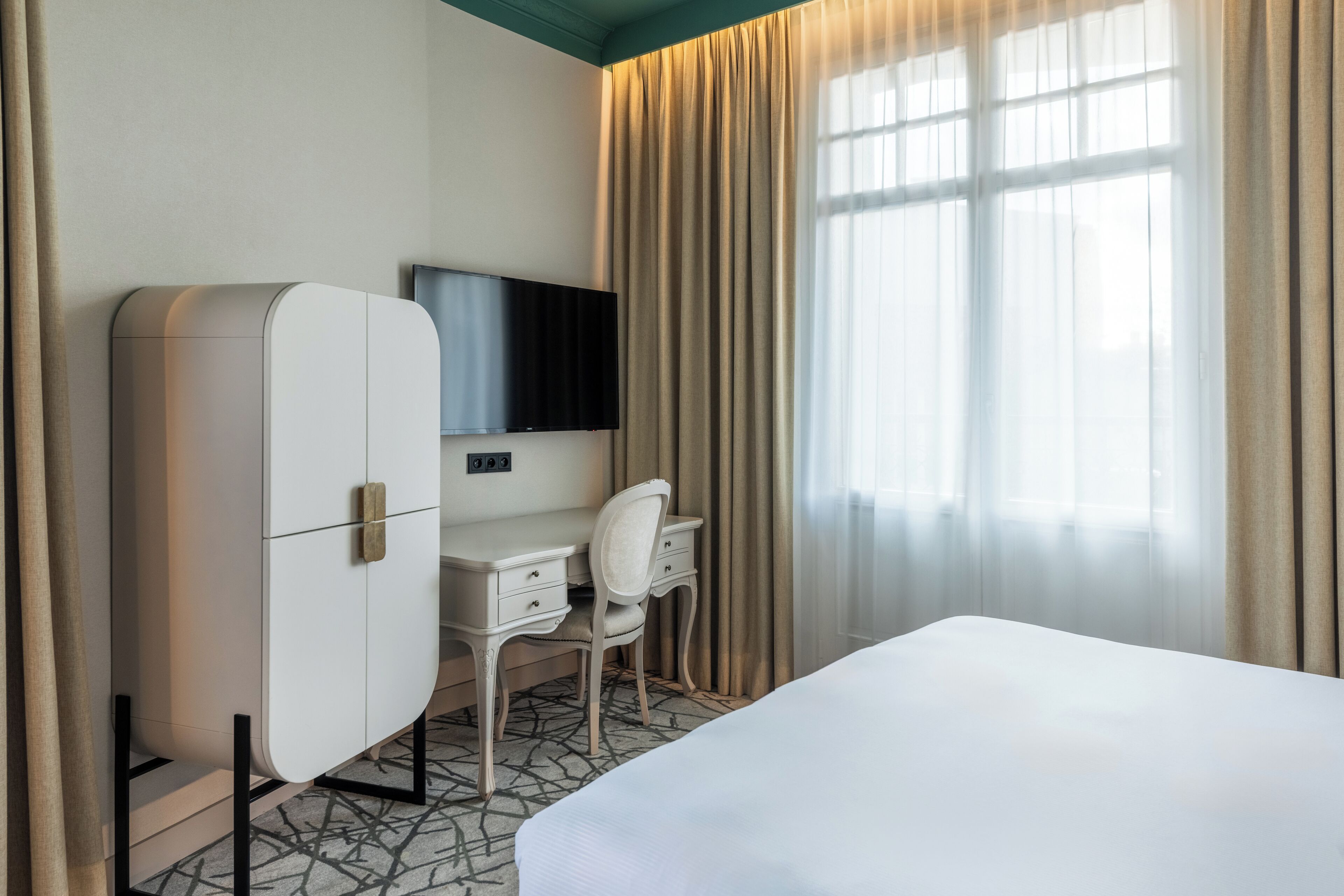 Una habitación de hotel con cama, escritorio, silla, televisor y armario.