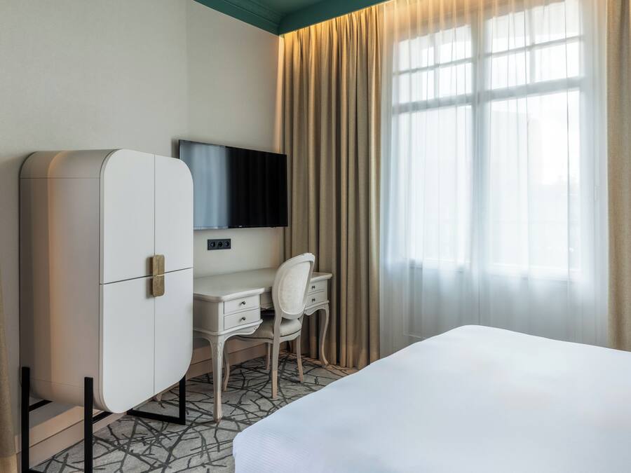 Una habitación de hotel con cama, escritorio, silla, televisor y armario.