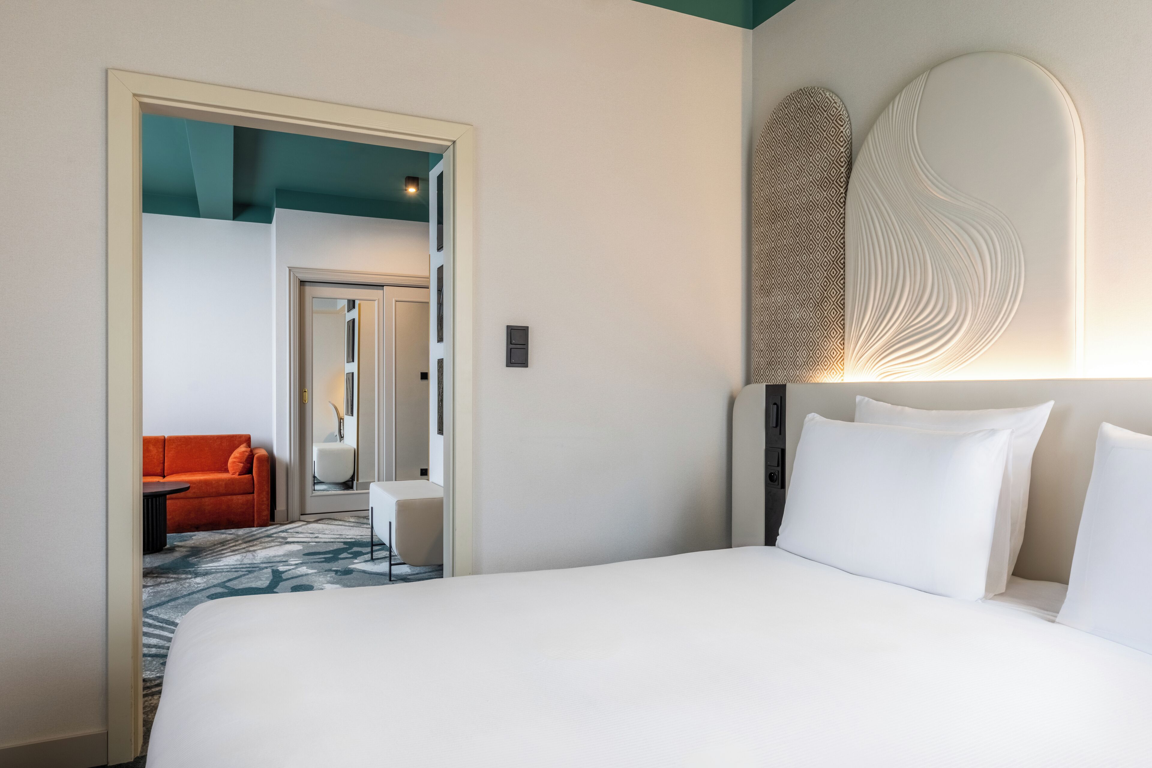 Ein Hotelzimmer mit einem großen Bett, einer Couch und einem kleinen Tisch. Eine Tür führt in einen weiteren Raum.