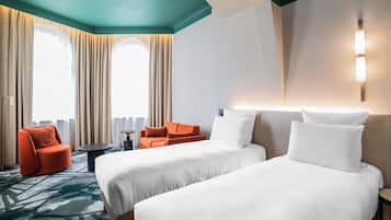 A hotel room with two beds, a red armchair, a small table, and a large window with curtains.