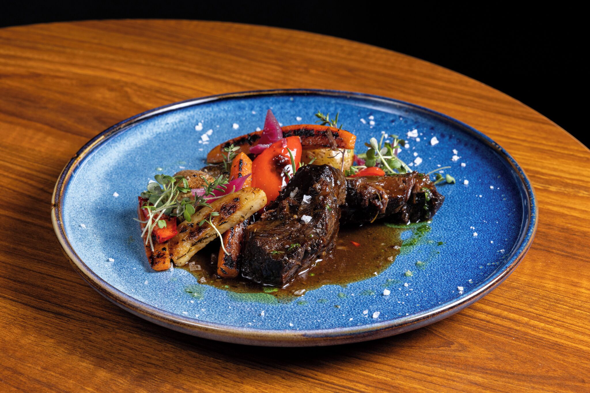 A blue ceramic plate with a steak and vegetables on a wooden table.