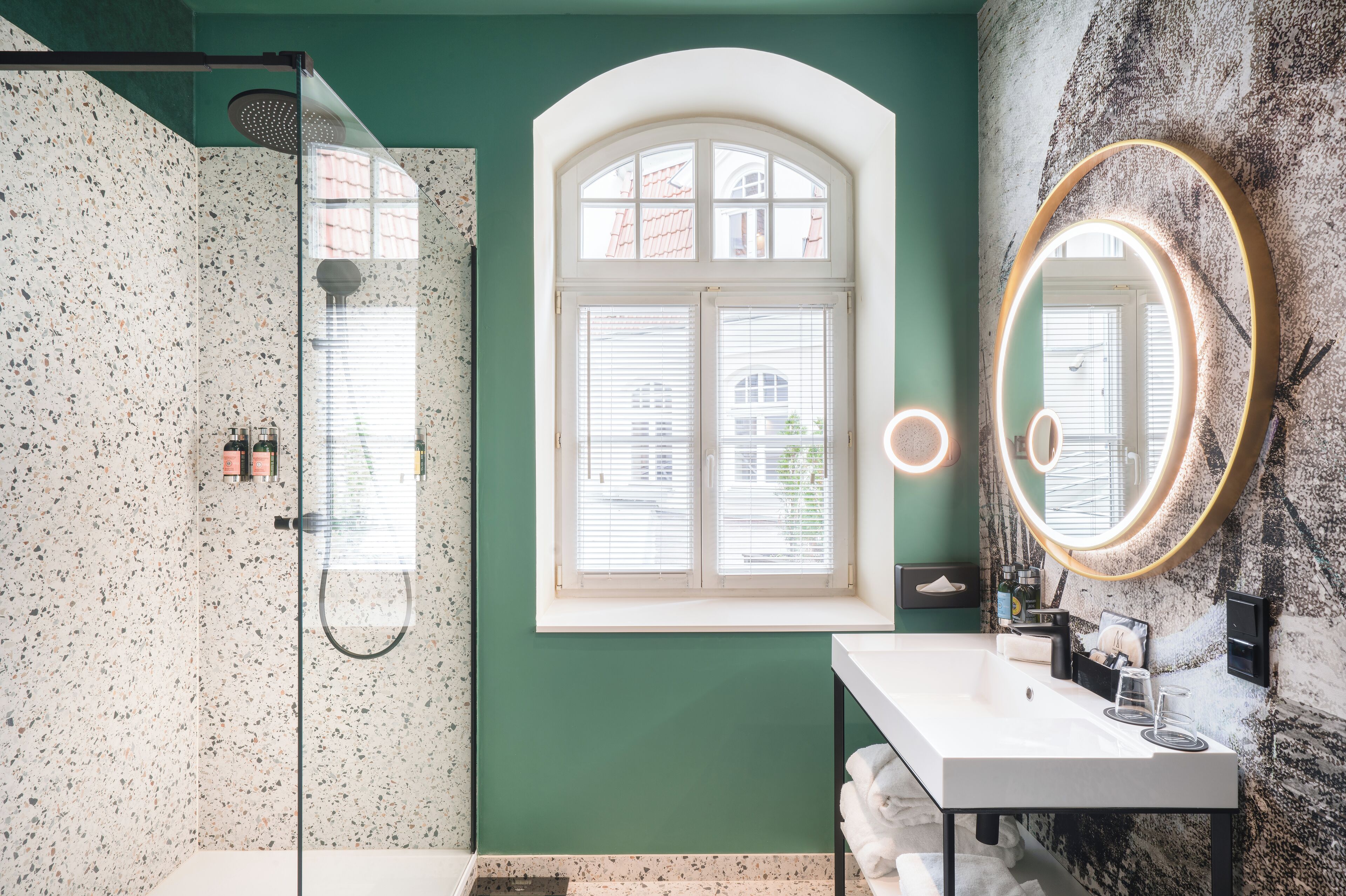 Un baño con ducha, tocador con espejo y ventana con persianas.