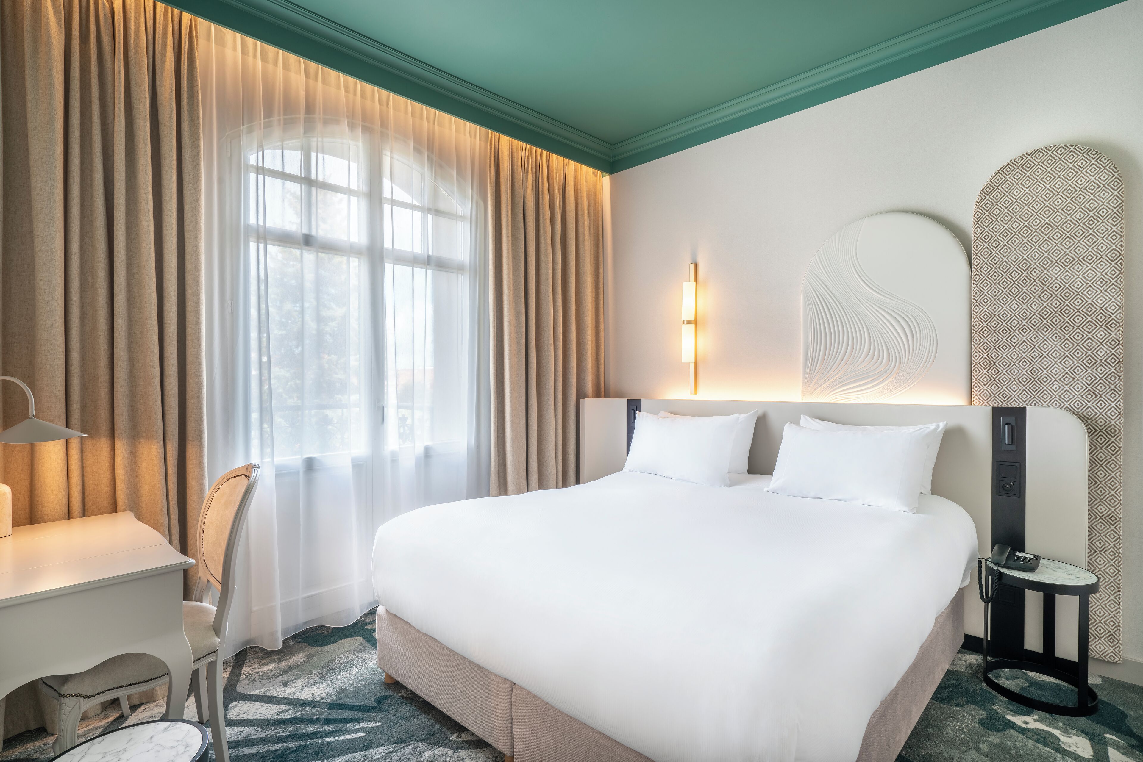 Ett hotellrum med en stor säng, ett skrivbord, en stol och ett litet bord.