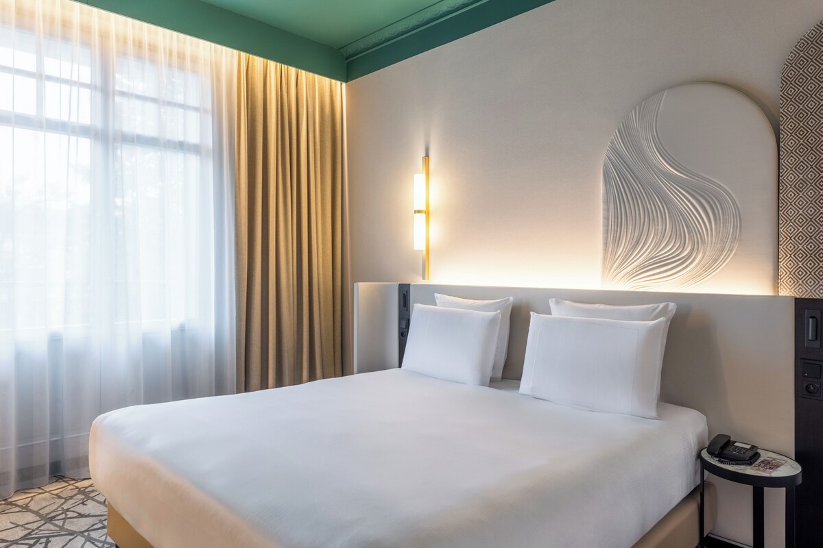 A hotel room with a large bed, a bedside table with a phone, and a wall-mounted light fixture.