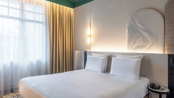 A hotel room with a large bed, a bedside table with a phone, and a wall-mounted light fixture.