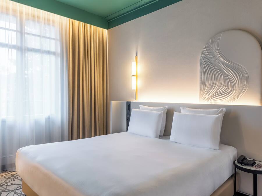 A hotel room with a large bed, a bedside table with a phone, and a wall-mounted light fixture.