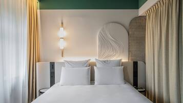 Quarto de hotel com uma cama grande, duas mesinhas de cabeceira, uma luminária fixada na parede e um objeto decorativo na parede.