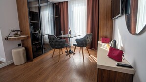 A modern hotel room with a dining area, a minibar, a television, and a red handbag on a table. - Navoris Hotel (Istanbul)
