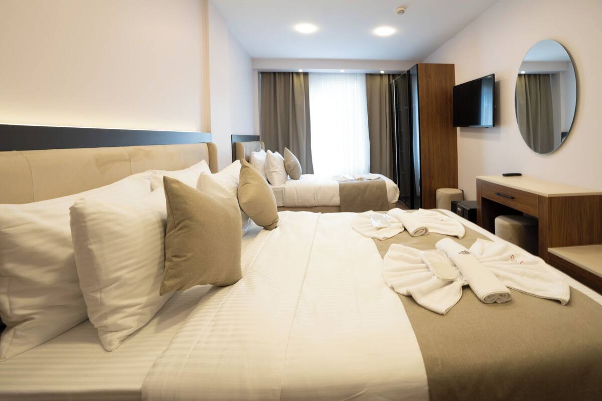 A hotel room with two beds, a desk, a mirror, and a TV.