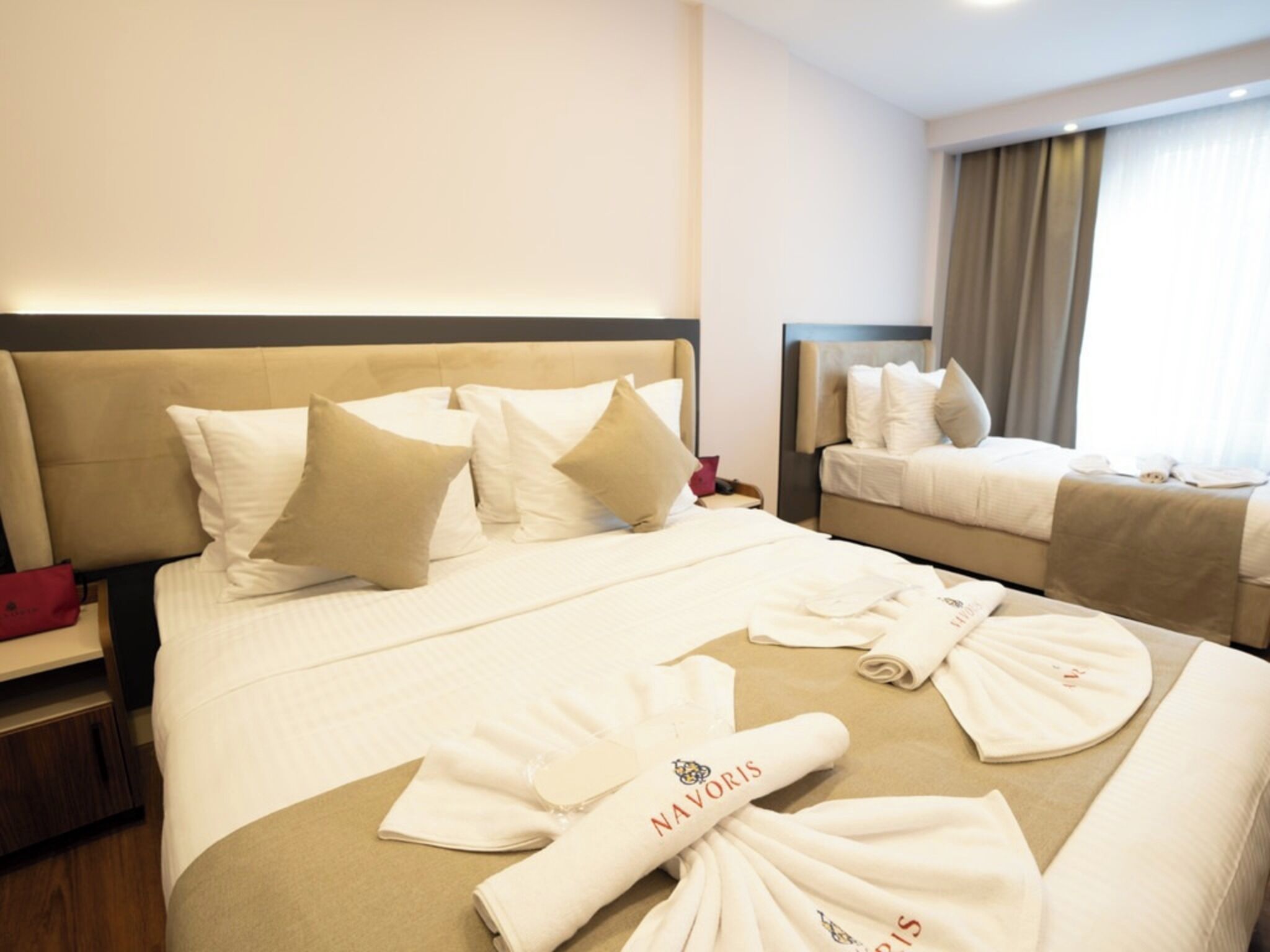 A hotel room with two beds, a nightstand, and a window with curtains.