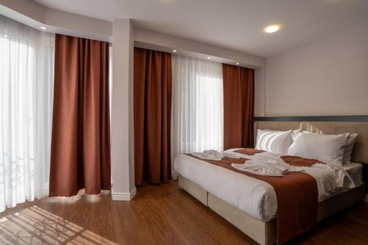 A hotel room with a bed, curtains, and a wooden floor.