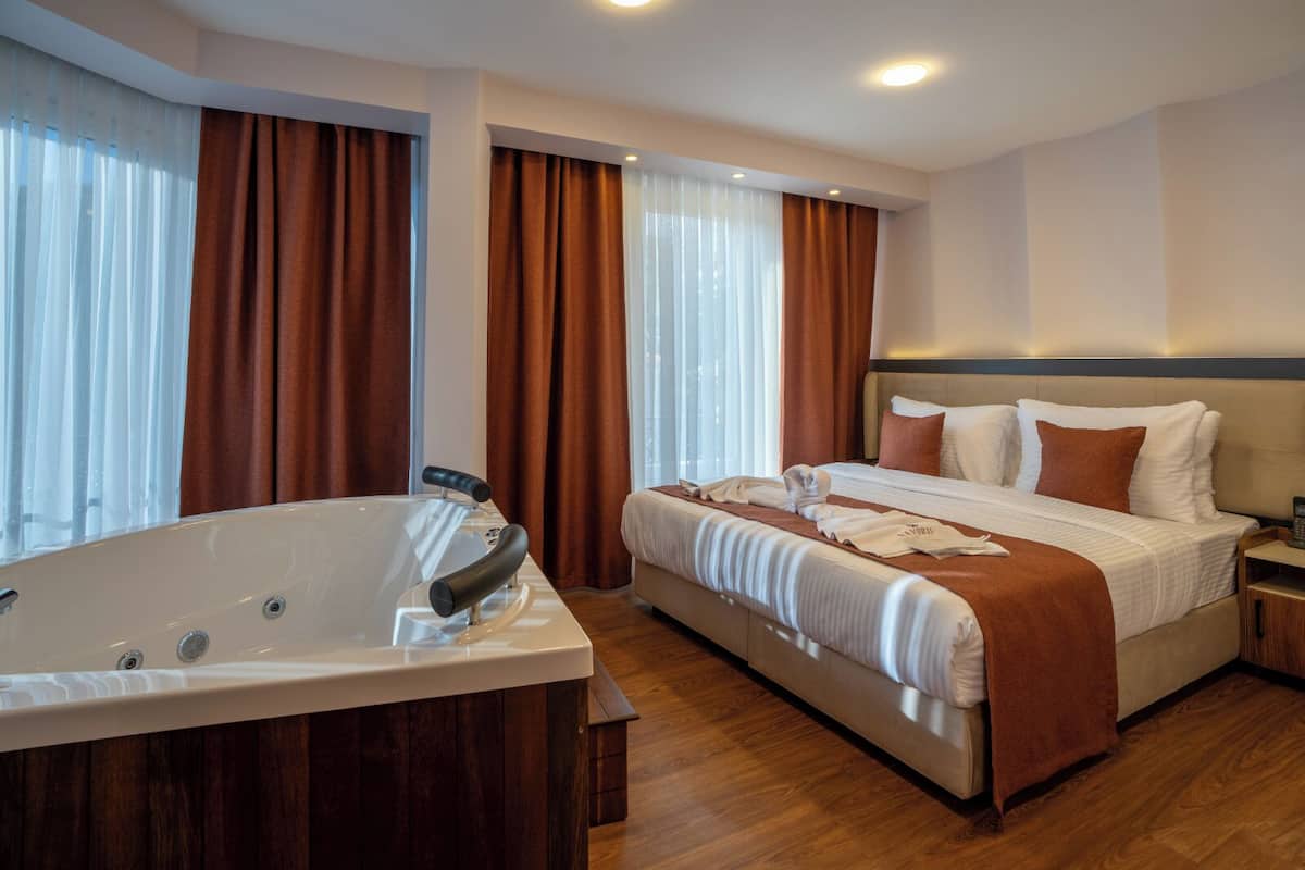 A modern hotel room with a large bathtub, a neatly made bed, and a wooden floor.