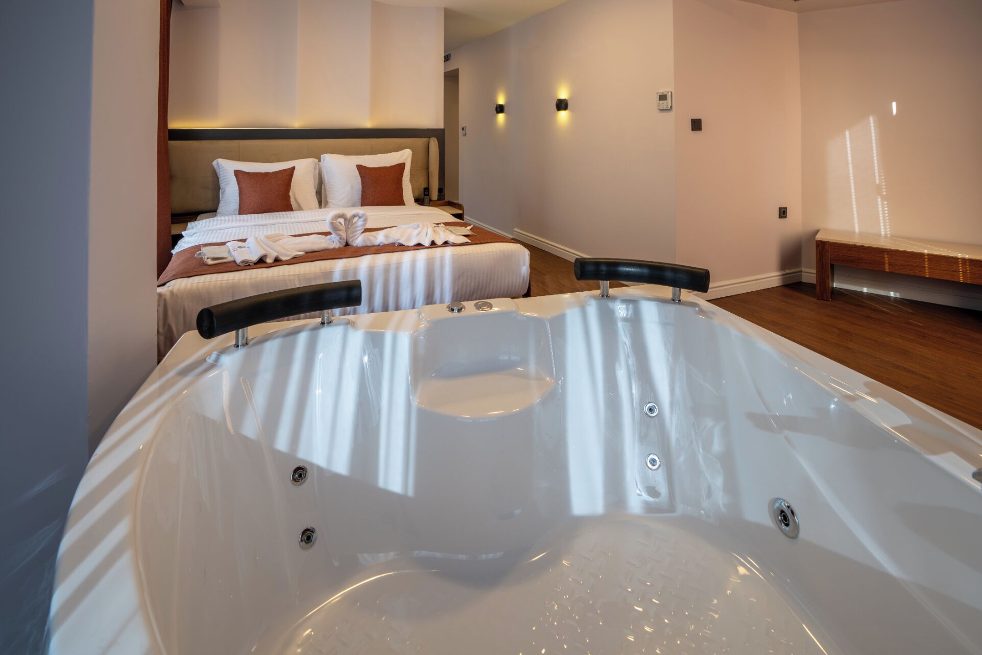 Una habitación de hotel moderna con una bañera grande, una cama con ropa de cama blanca y marrón, y un cabecero.