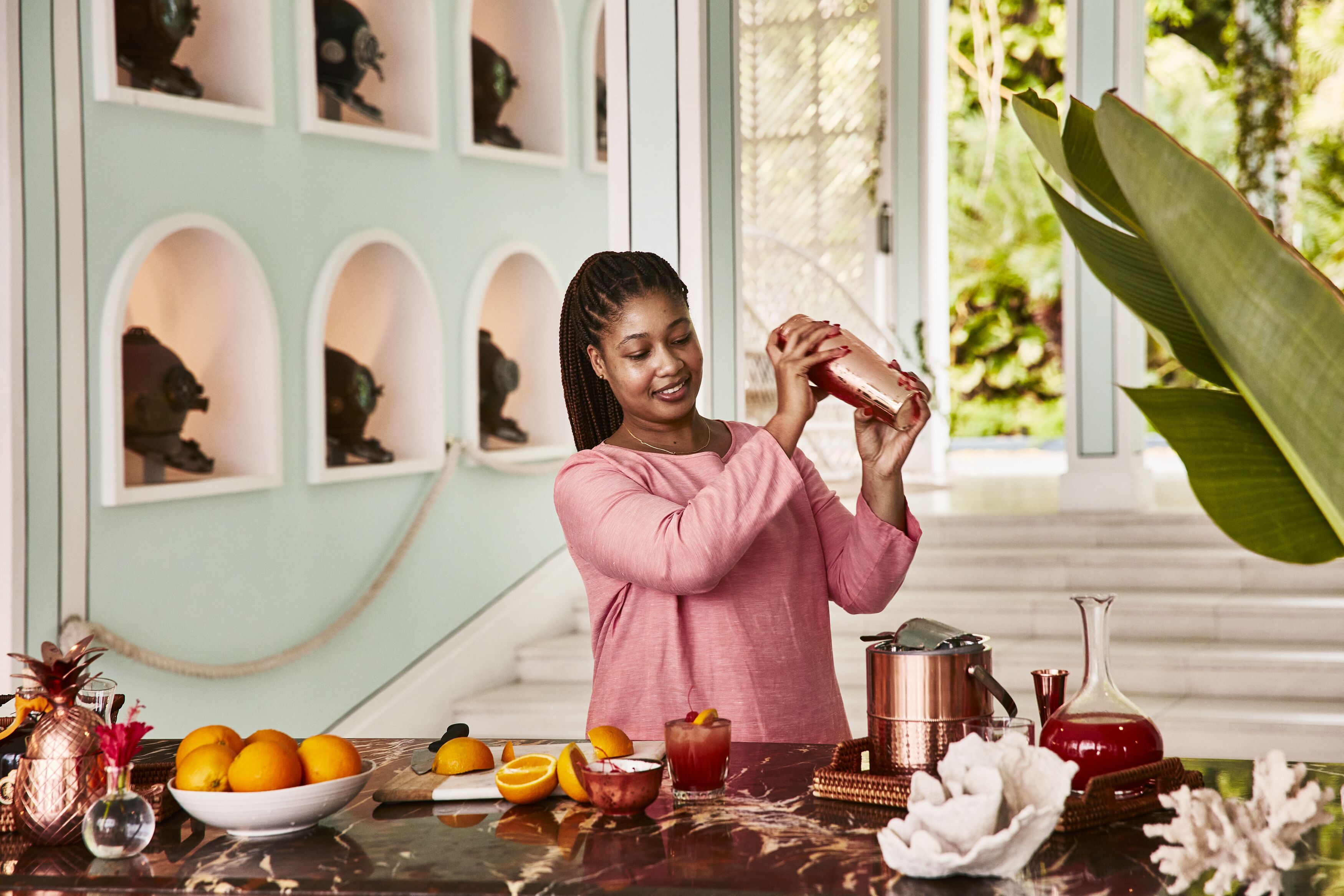 A person pouring a drink into a glass at a table with fruits and a copper pot.