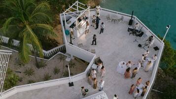 An outdoor wedding setup with a white tent, tables, and chairs, overlooking a beach and ocean.