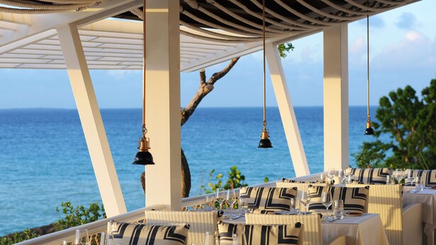 Un restaurante frente al mar con mesas preparadas para comer, con vista al océano.