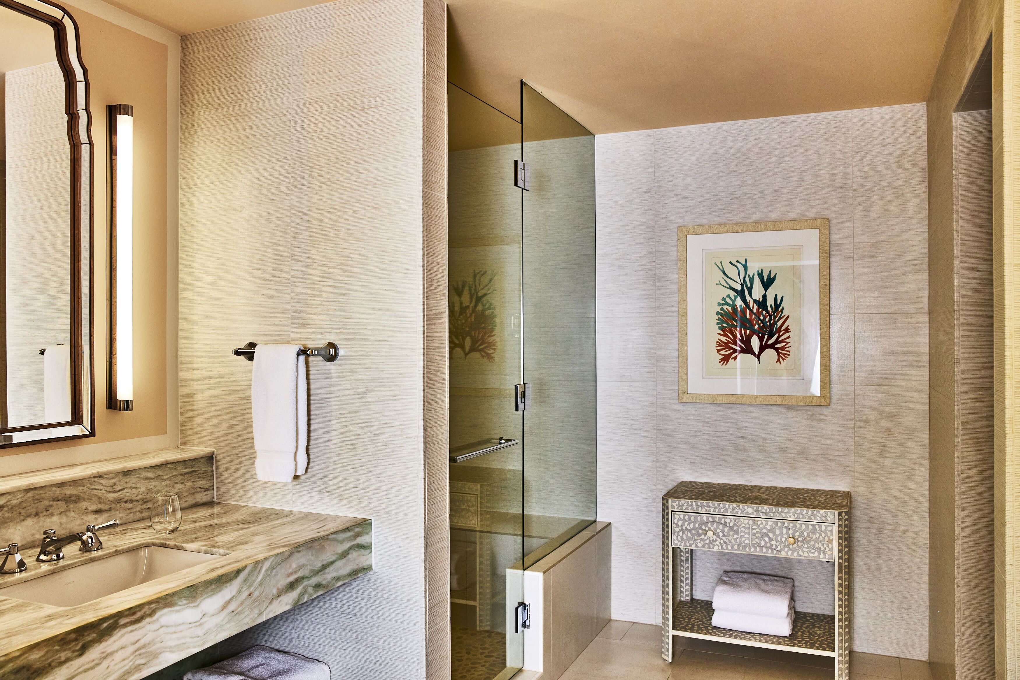 Une salle de bain moderne avec un lavabo en marbre, une douche en verre et une œuvre d’art encadrée au mur.
