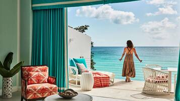 Une pièce avec vue sur la mer, un mur blanc, une chaise à motifs rouges, une chaise blanche et une table blanche.