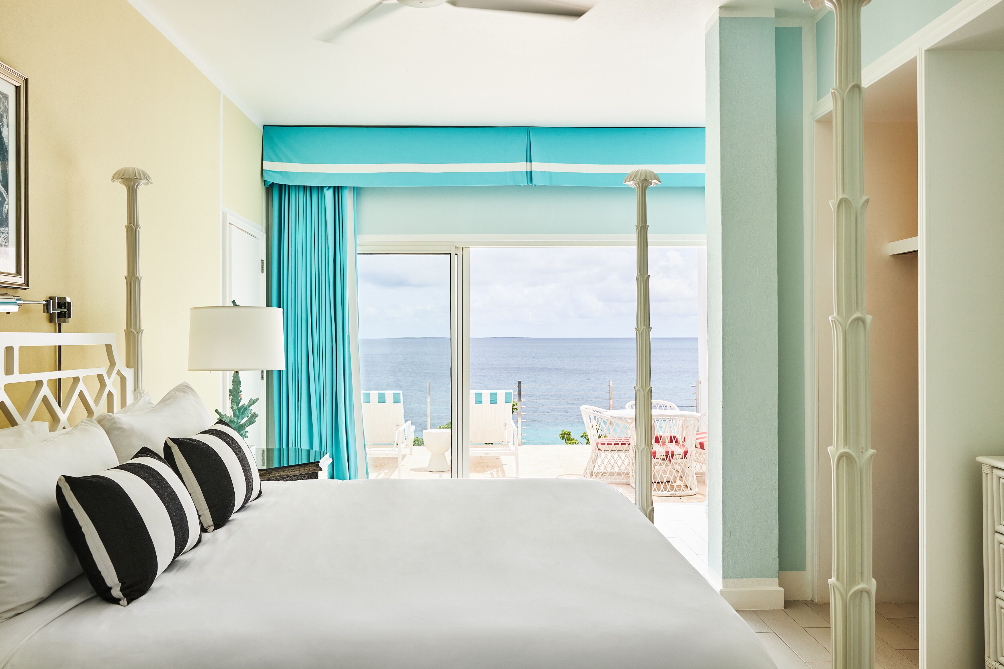A hotel room with a large bed, a view of the sea, and a balcony with outdoor seating.
