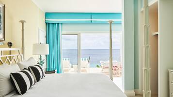 A hotel room with a large bed, a view of the sea, and a balcony with outdoor seating.