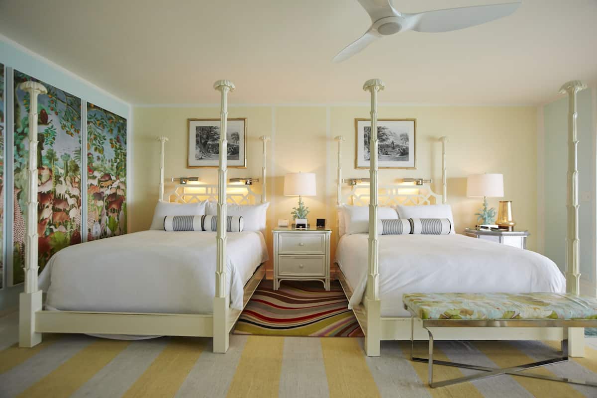 A four-poster bed with a striped rug, a bench, and two bedside tables with lamps.