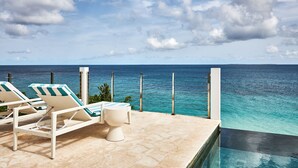 Zona junto a la piscina con sillones de descanso y vista al océano.