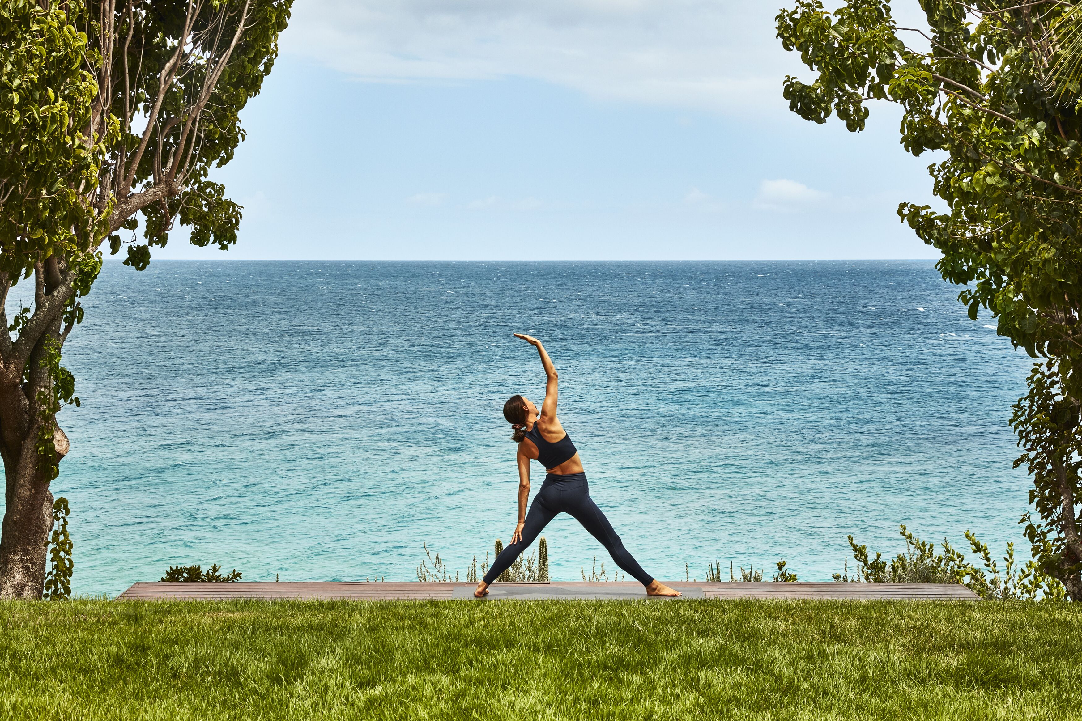 A person performing a yoga pose on a wooden deck with a view of the ocean.