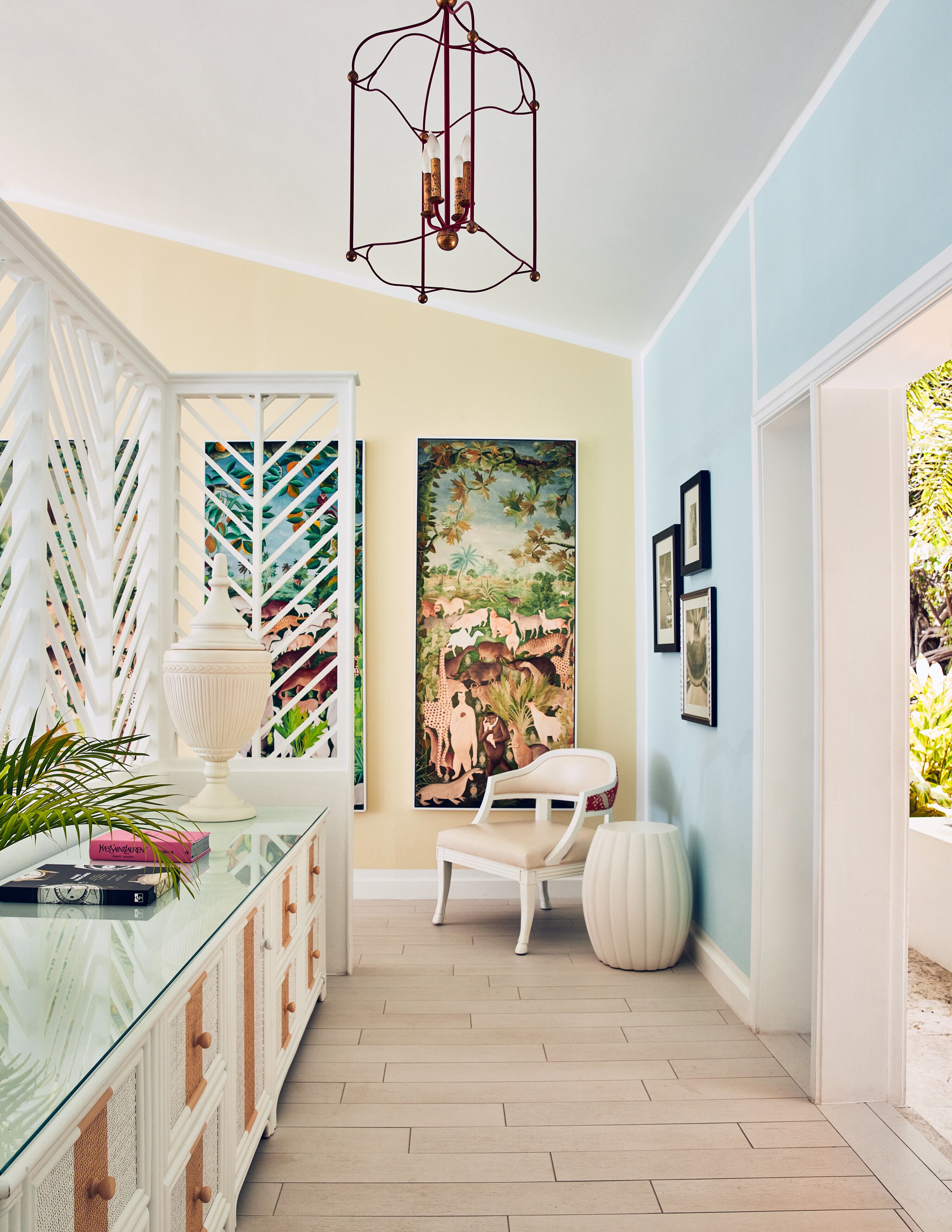 A hallway with a glass cabinet, a white chair, a large painting, and a hanging light fixture.