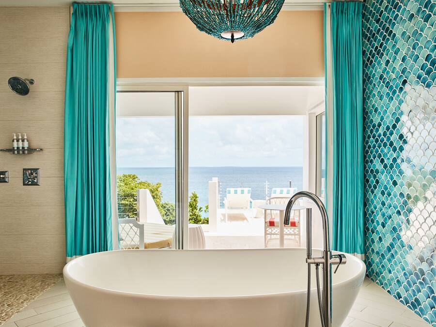 A modern bathroom with a large bathtub, a shower, and a view of the sea.