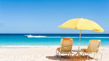 A beach with two lounge chairs and a yellow umbrella.