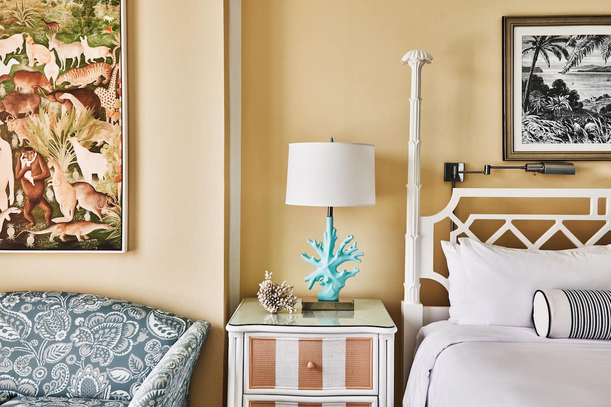 A bedroom with a bed, a nightstand with a lamp, a framed picture, and a wall painting.