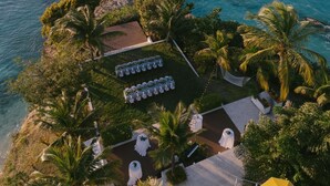 Vista aérea de un resort con acceso directo a la playa, que incluye una zona de estar con mesas y sillas, palmeras y vistas al océano.