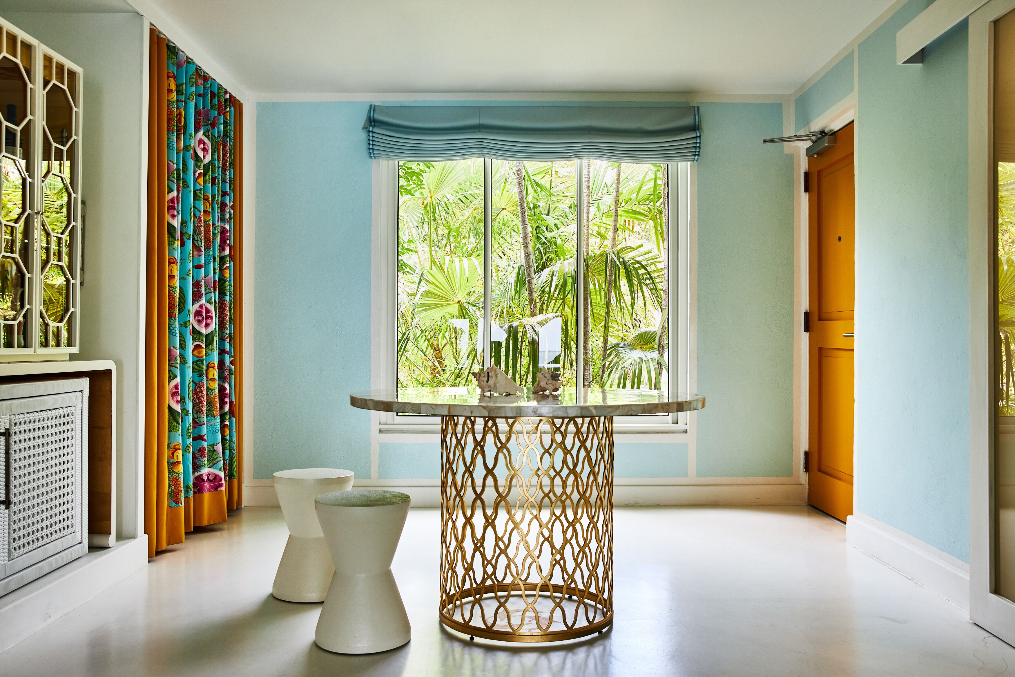 Una habitación con una mesa redonda, un pedestal blanco y una ventana con vistas a zonas verdes.