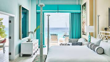 A bedroom with a large bed, a view of the ocean, a balcony with a table and chairs, and a door leading outside.