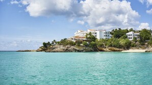 Un hotel costero con varias edificaciones blancas, rodeado de abundante vegetación y un mar turquesa cristalino.