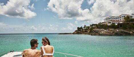 A couple on a boat with a view of a coastal building and rocky shoreline.