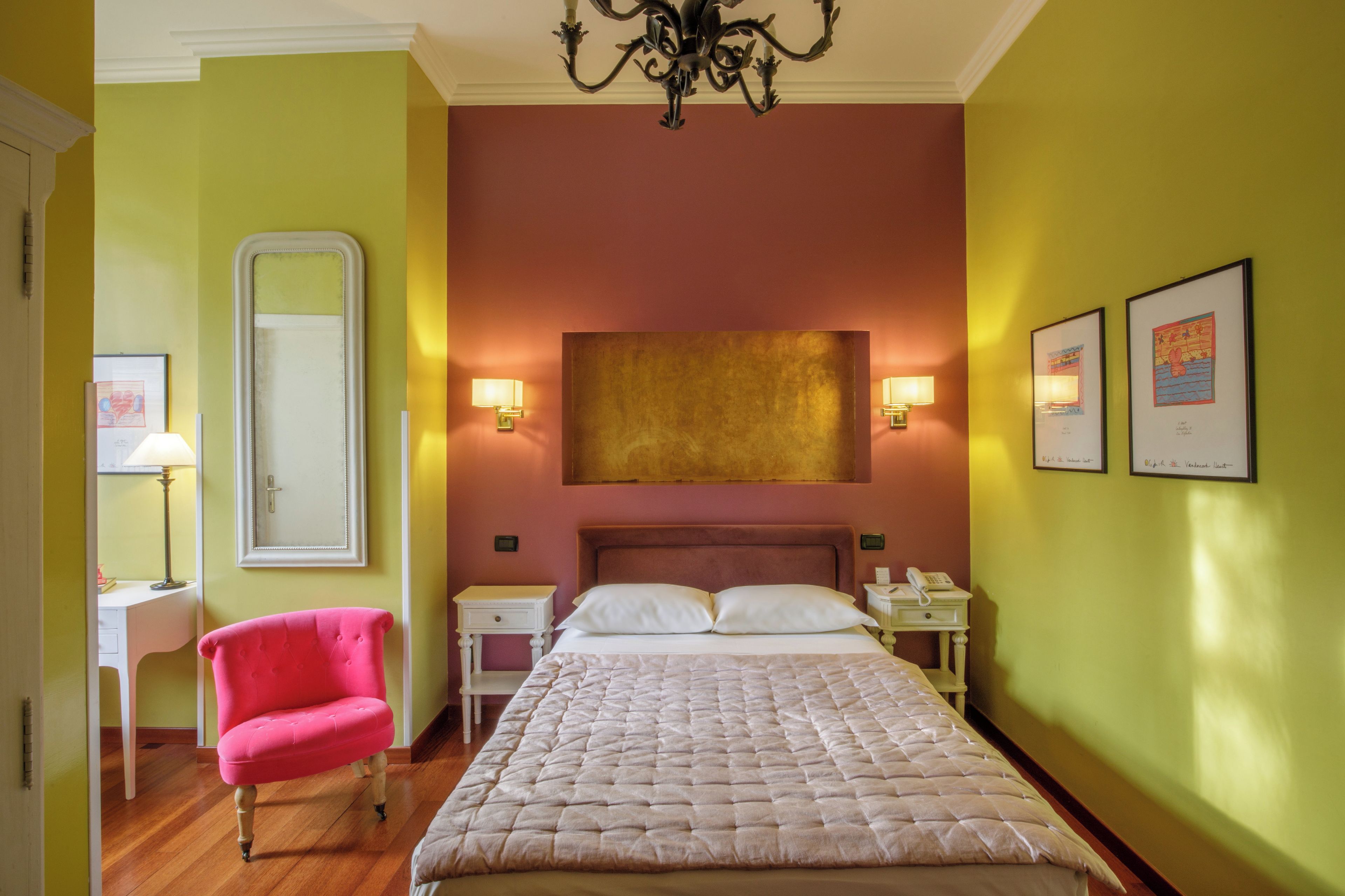 A hotel room with a bed, a chair, a desk, a nightstand, a mirror, and wall art.