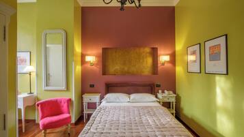 A hotel room with a bed, a chair, a desk, a nightstand, a mirror, and wall art.