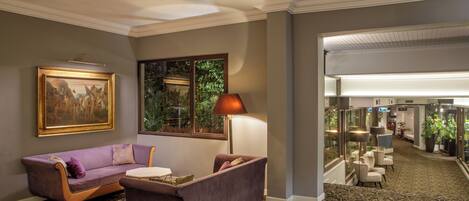 A lobby with a purple sofa, a table, a lamp, a painting, and a view of greenery through a window.