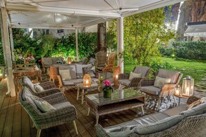 En udendørs terrasse med fletmøbler, et glasbord og en lygte.